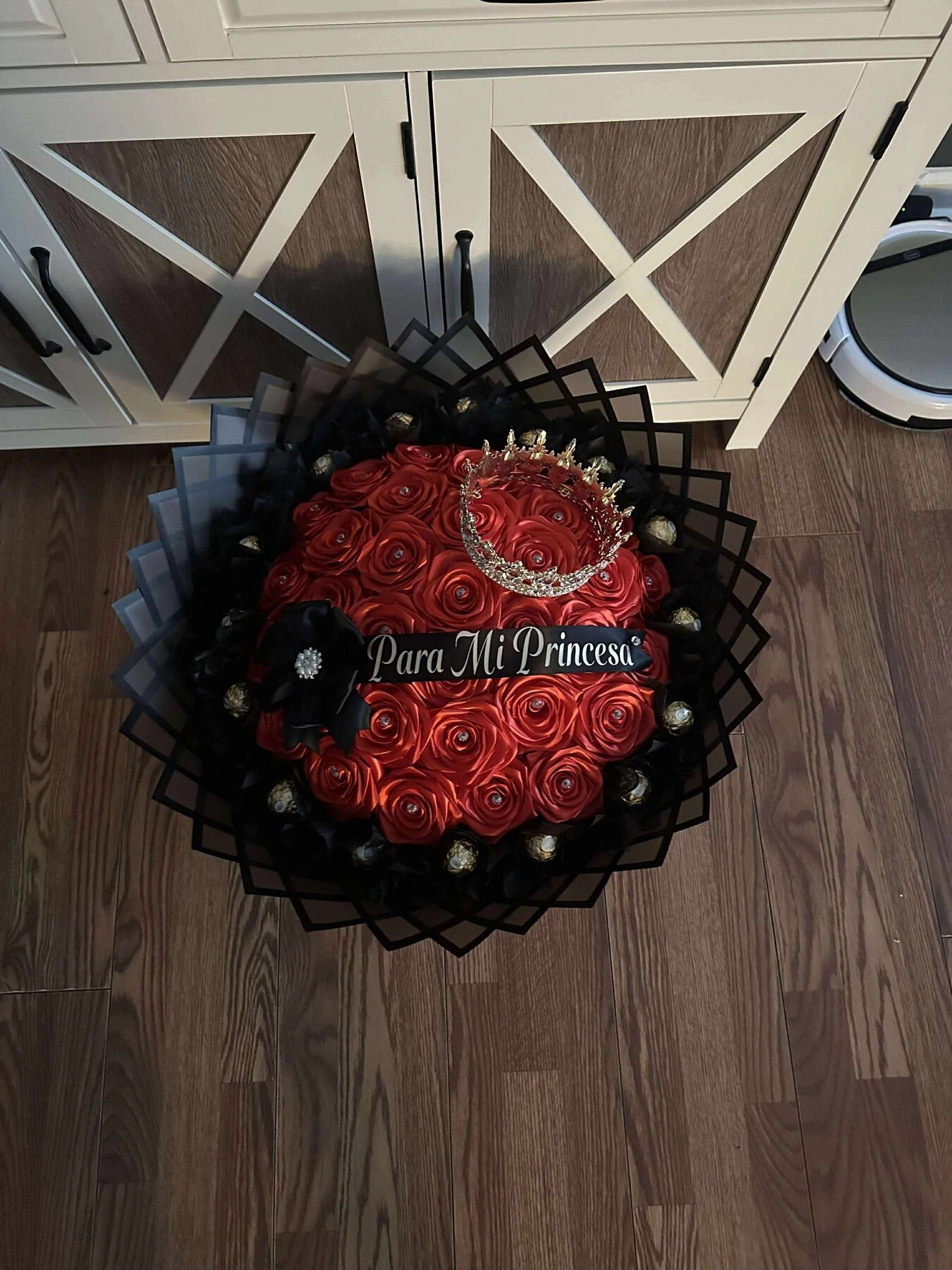 A red floral arrangement with dark layered wrapping and a pale ribbon.