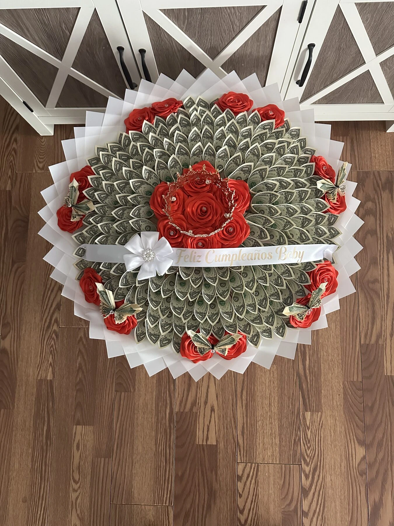 A round arrangement of folded bills with a red floral center and pale wrapping.