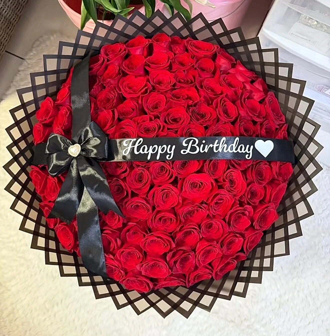 A round arrangement of red rose-shaped blooms with black geometric wrapping and a center ribbon.