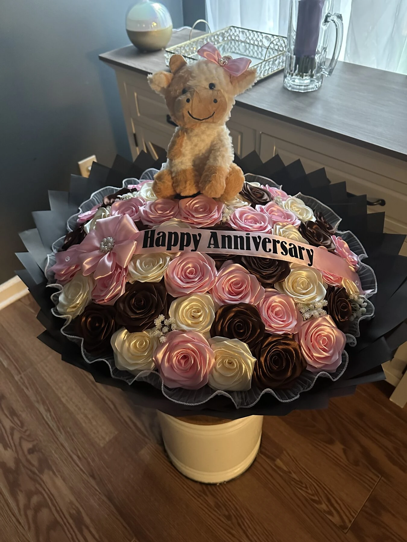 A plush animal above a tiered arrangement of pink and cream blooms.