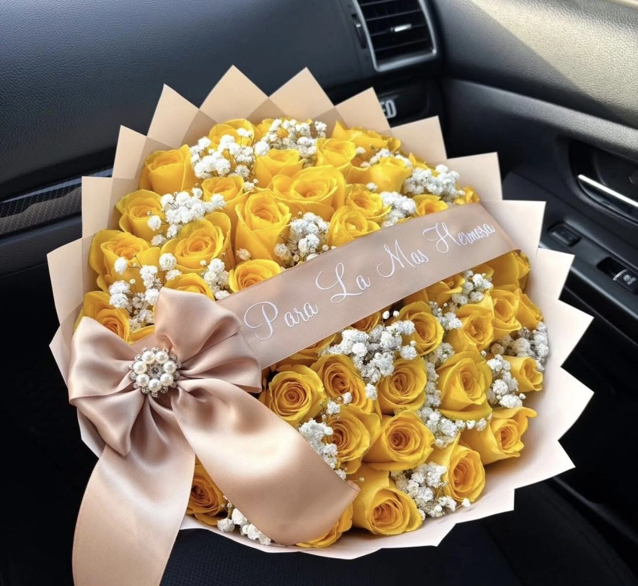 Yellow rose-shaped blooms with small white flowers, pale wrapping, and a wide blush bow.