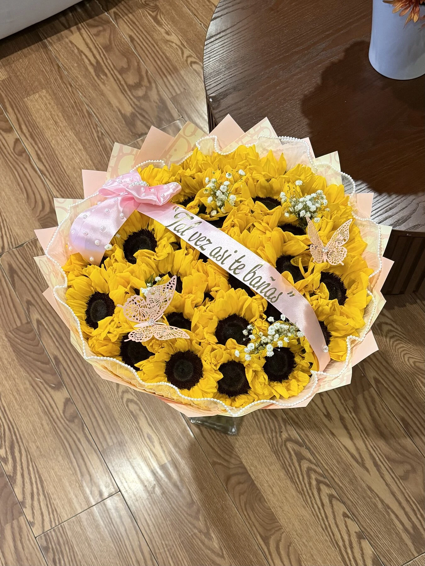 A yellow and white floral arrangement with sunflowers, pale wrapping, and a ribbon.