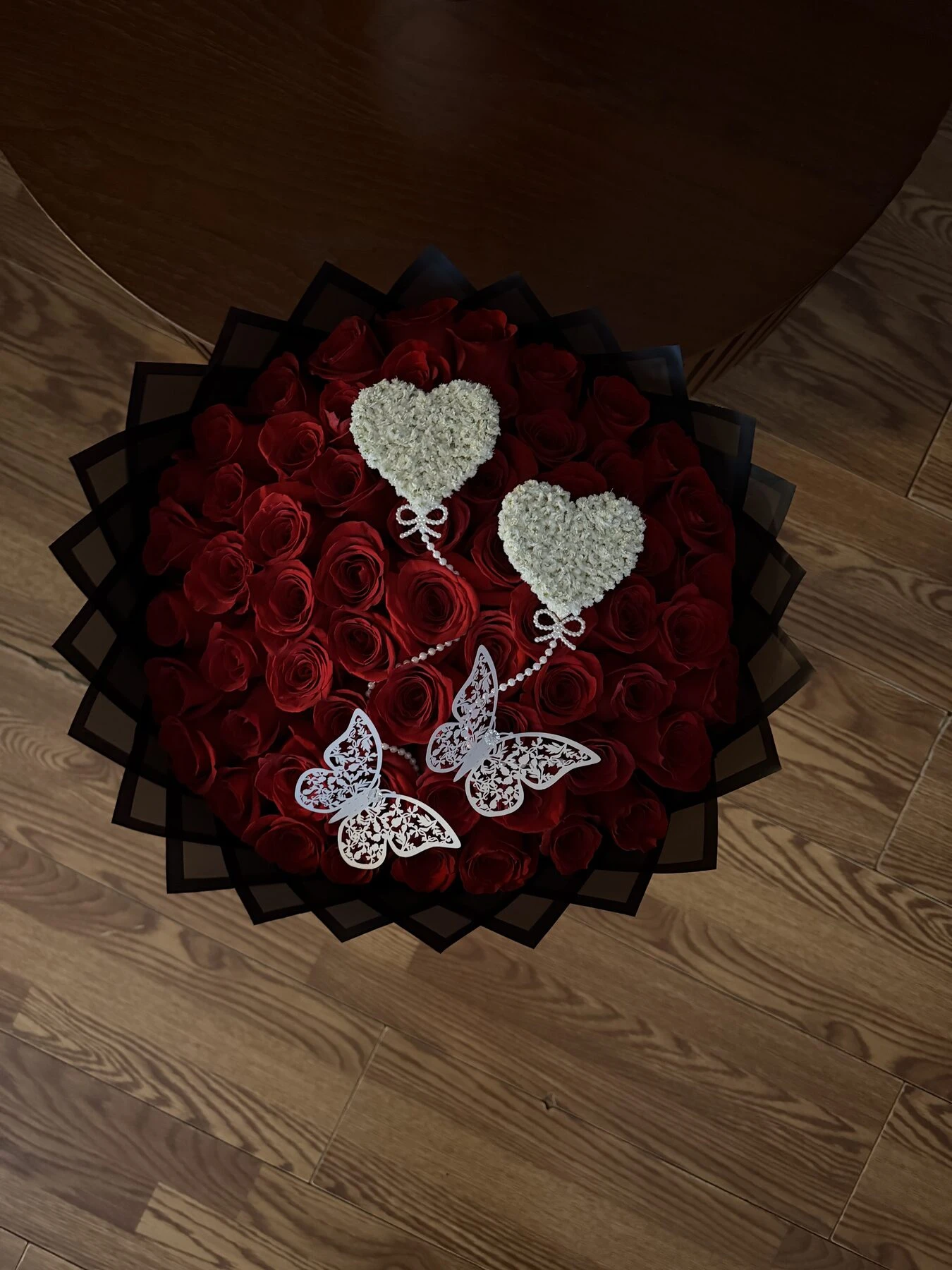 A red floral arrangement with two white heart ornaments and butterfly decorations.