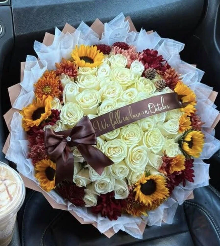 A full arrangement of cream blooms with yellow and orange accents and a dark bow.