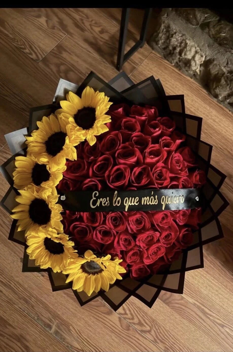 Red blooms and sunflowers arranged in a circle with dark wrapping and a center ribbon.