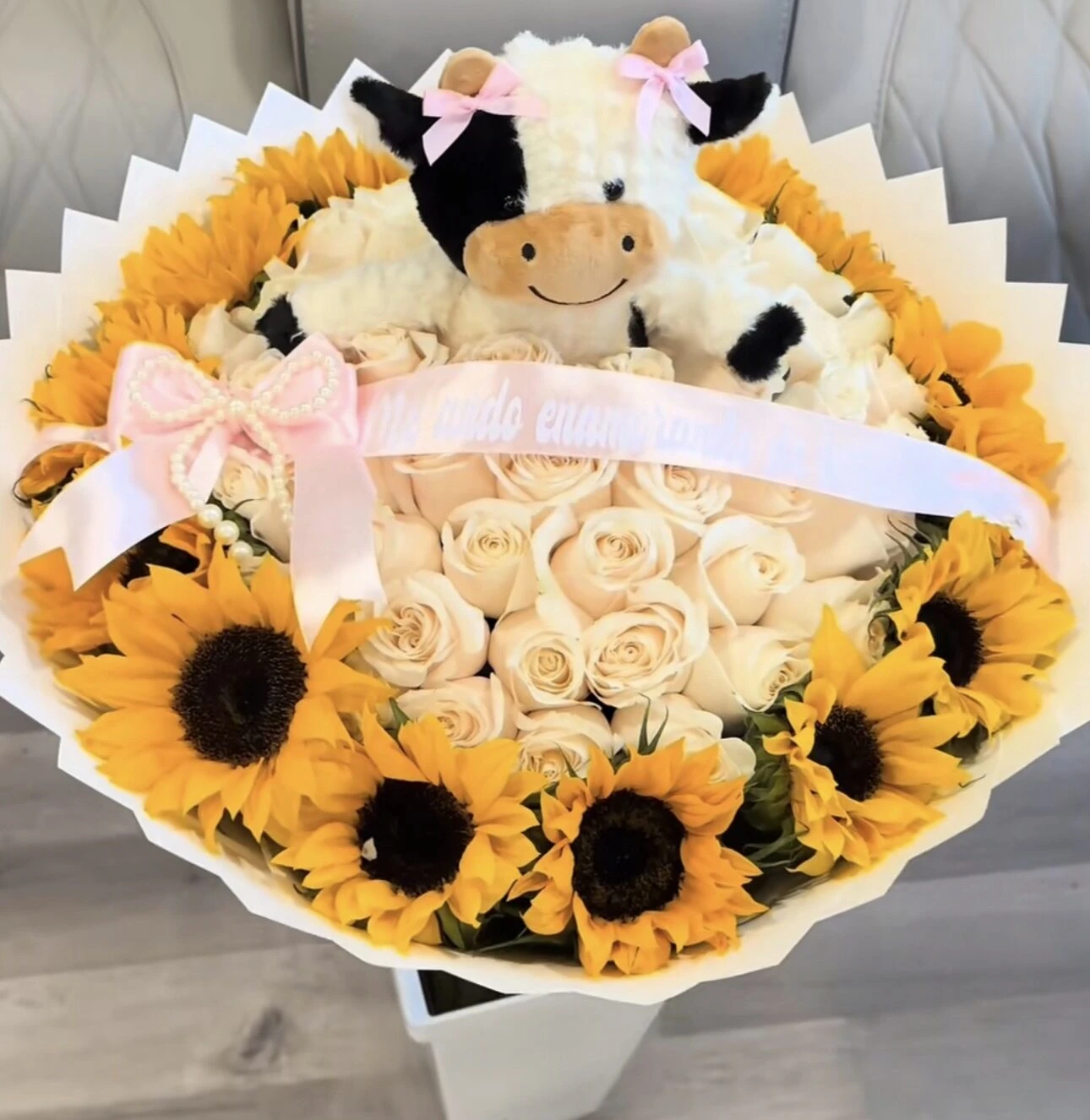 A white and yellow floral arrangement topped with two small plush animals.