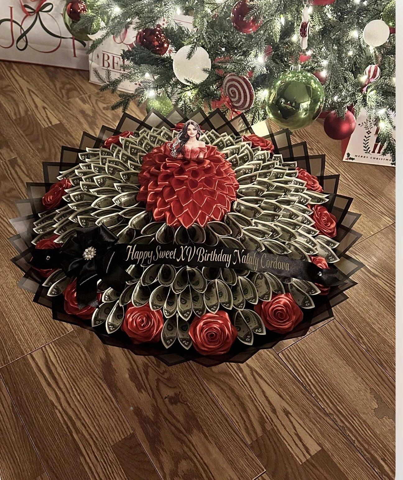 A red round arrangement with dark wrapping and decorative greenery in the background.