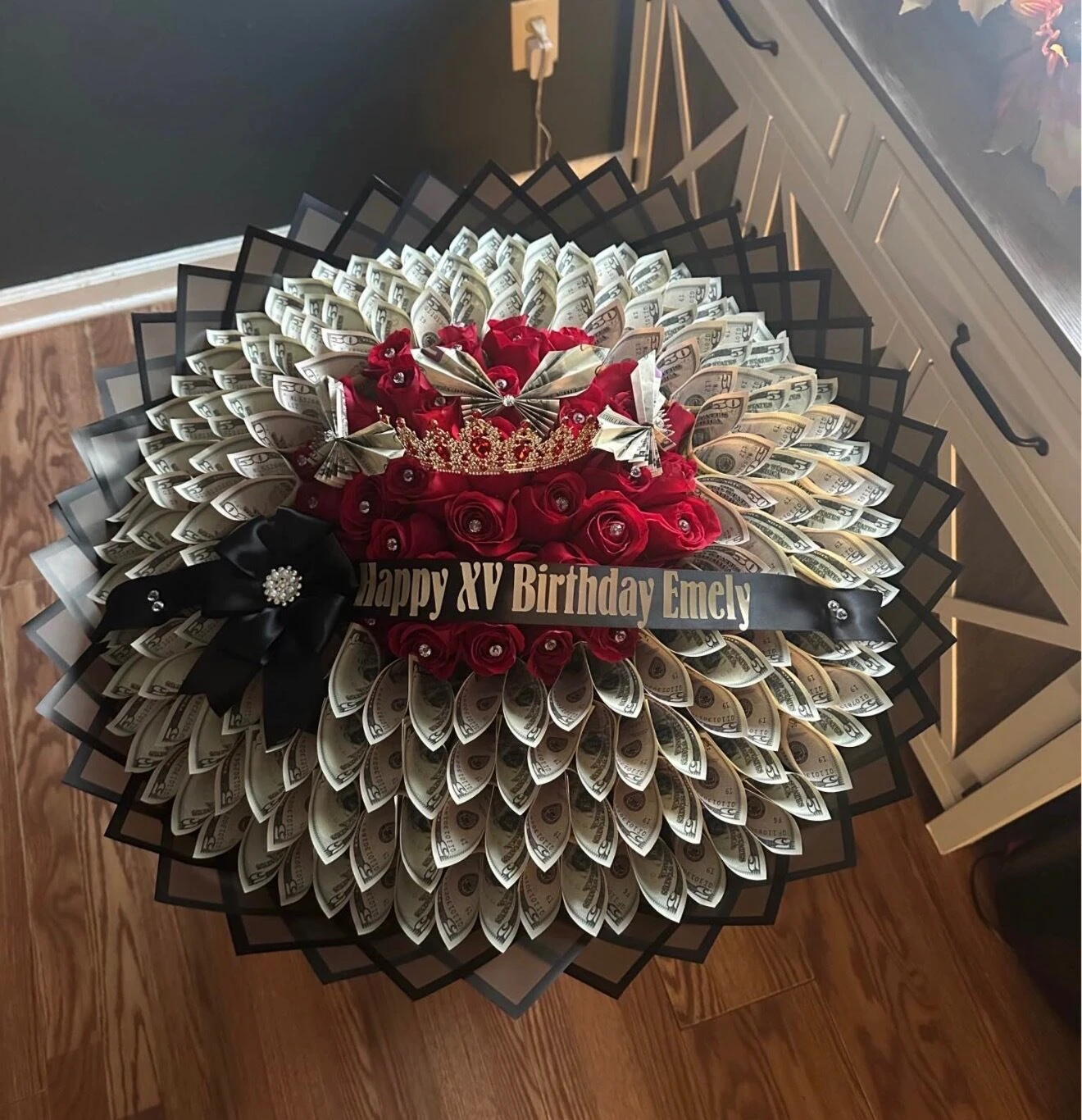A red floral arrangement with folded bills, pale wrapping, and a ribbon across the center.