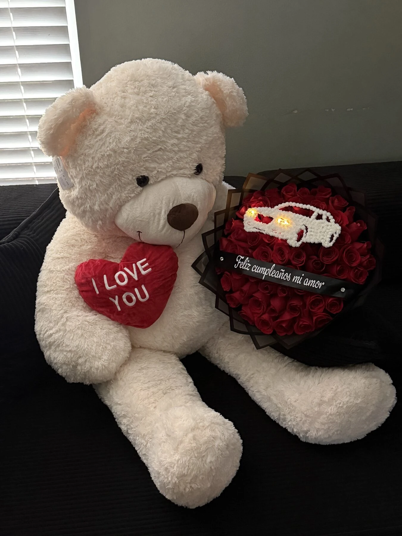A white plush bear beside a dark red arrangement with pale wrapping.
