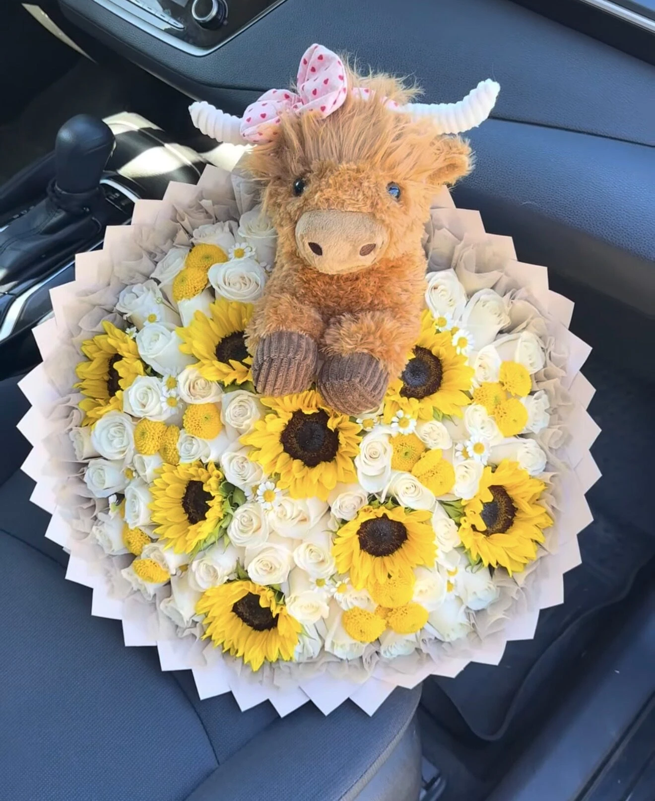 A small plush animal above a yellow and white flower arrangement.