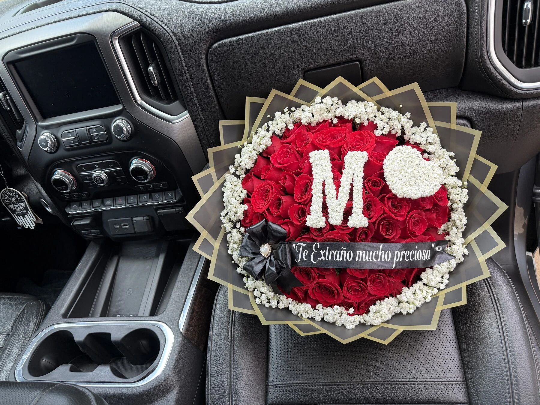 A red floral arrangement with a pale letter at the center, photographed inside a car.