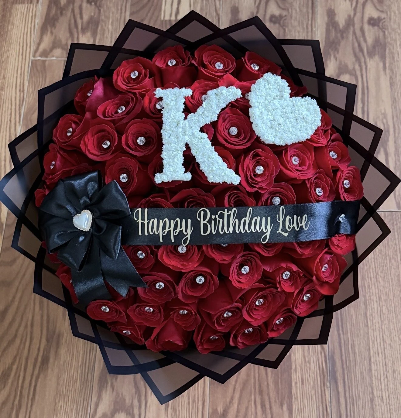 A red floral arrangement with a large pale blue letter, heart, and ribbon.