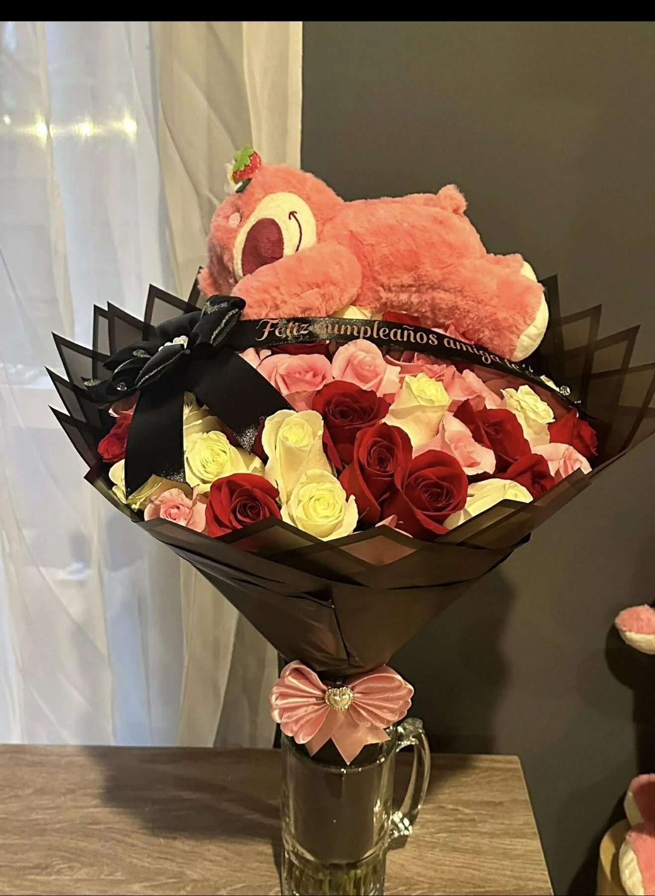 A pink plush bear above a bouquet of red, white, and pink flowers.