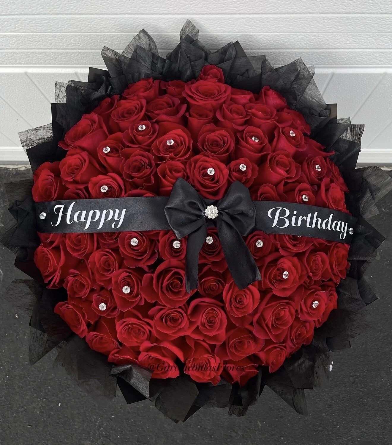 A round red floral arrangement with a dark ribbon against a pale background.
