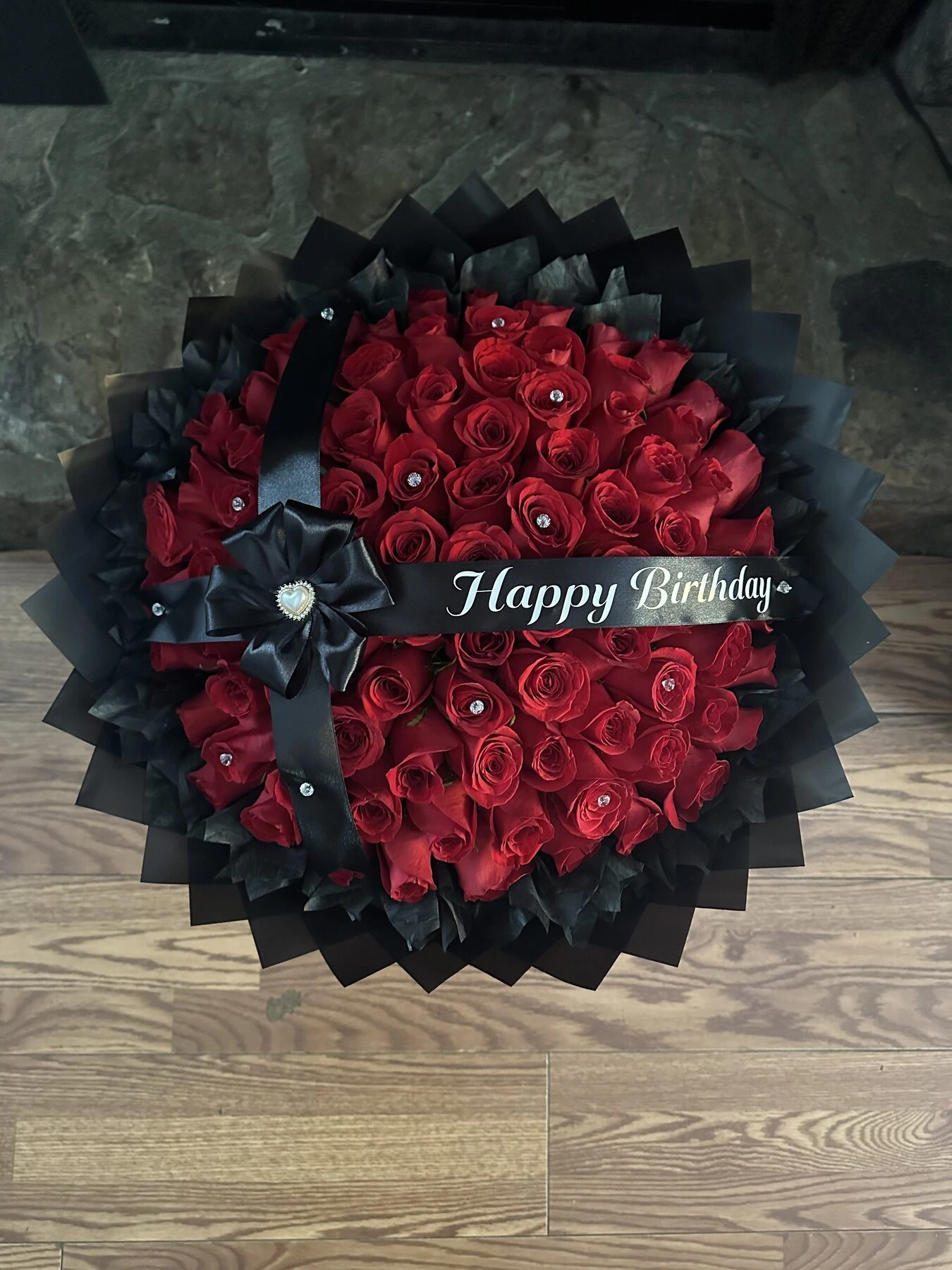 A dark circular arrangement with red blooms at the center and folded bills around the edge.