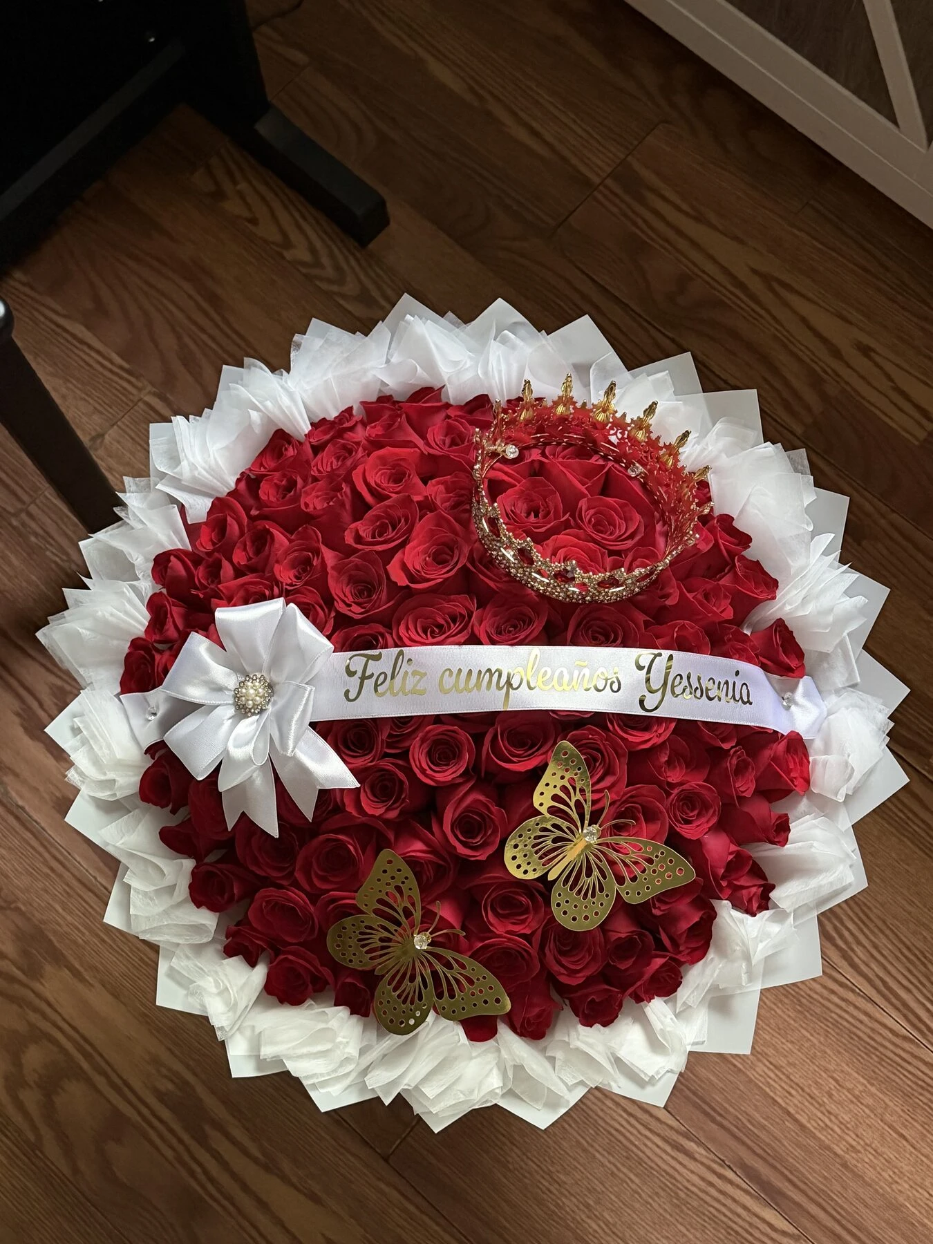 A round red floral arrangement with pale wrapping, small white blooms, and decorative accents.