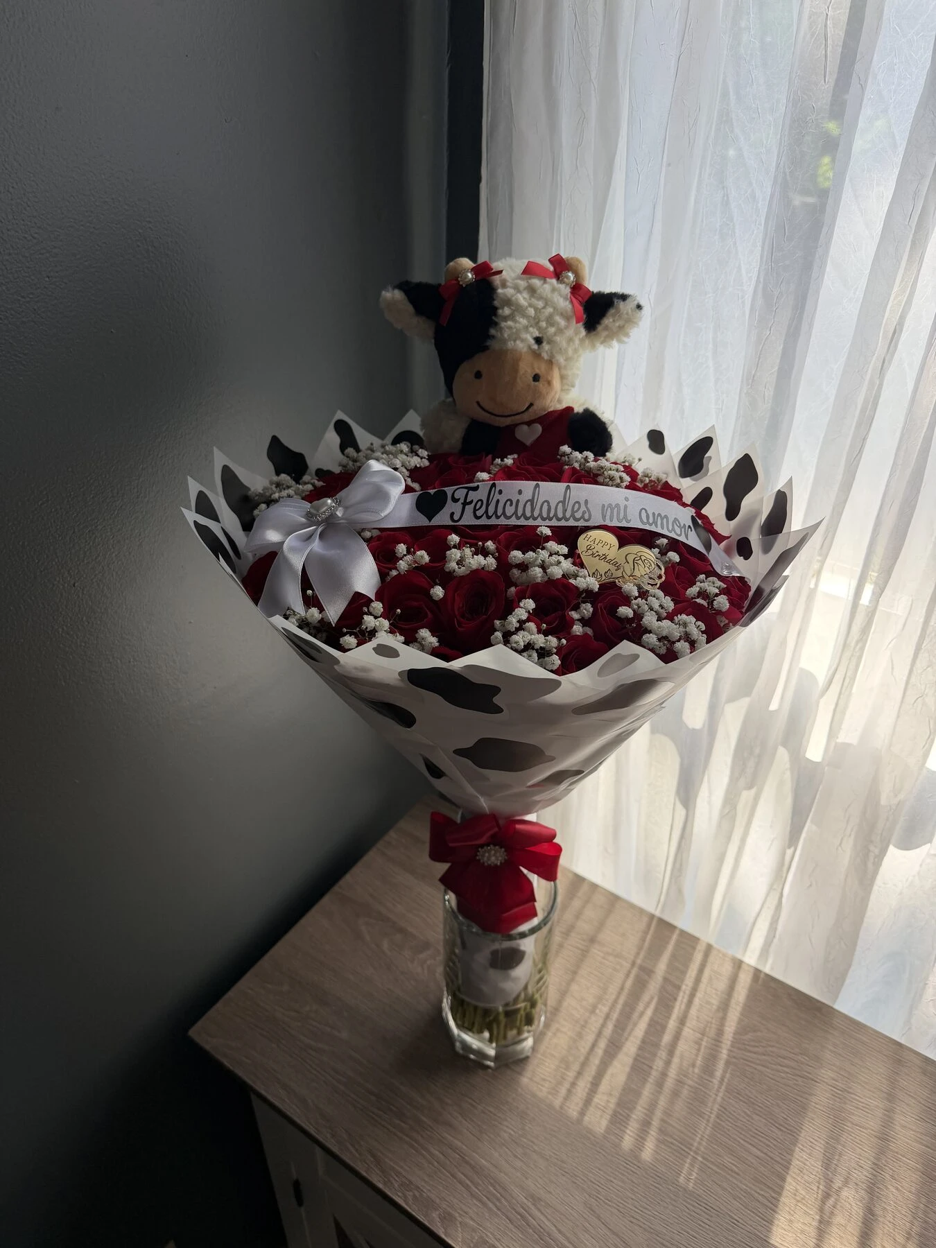 A small red and white arrangement with a plush cow above the flowers.