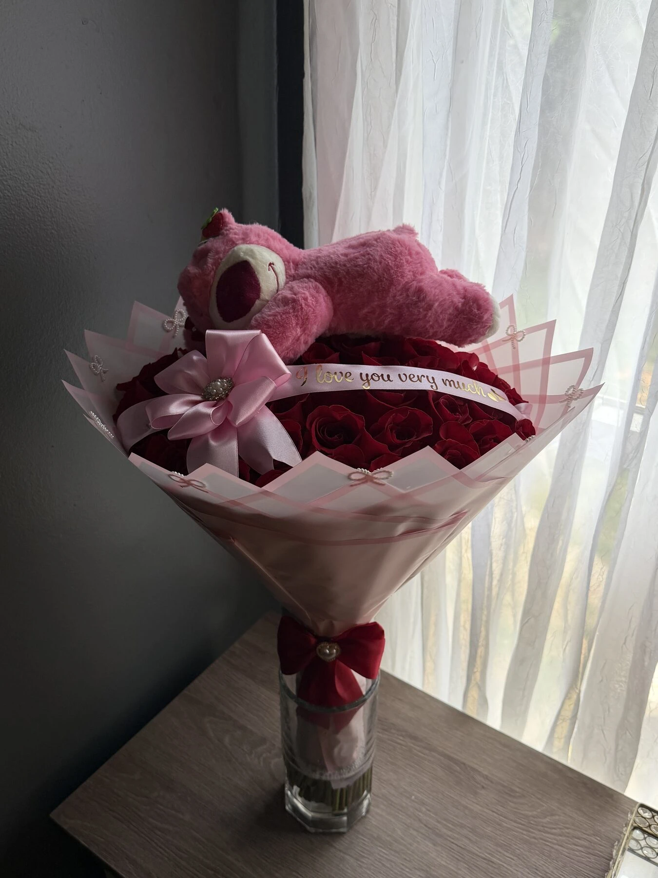 A pink and red arrangement in a vase with a small plush toy at the center.
