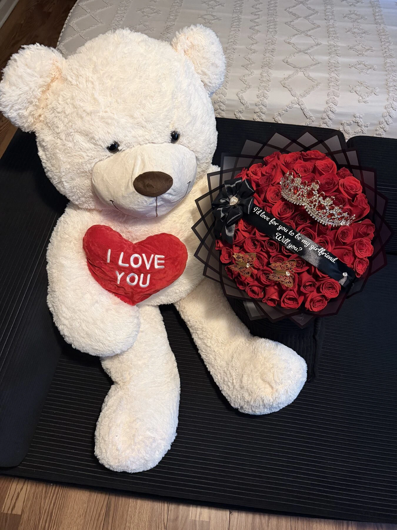 A white plush bear beside a round red arrangement with dark wrapping.